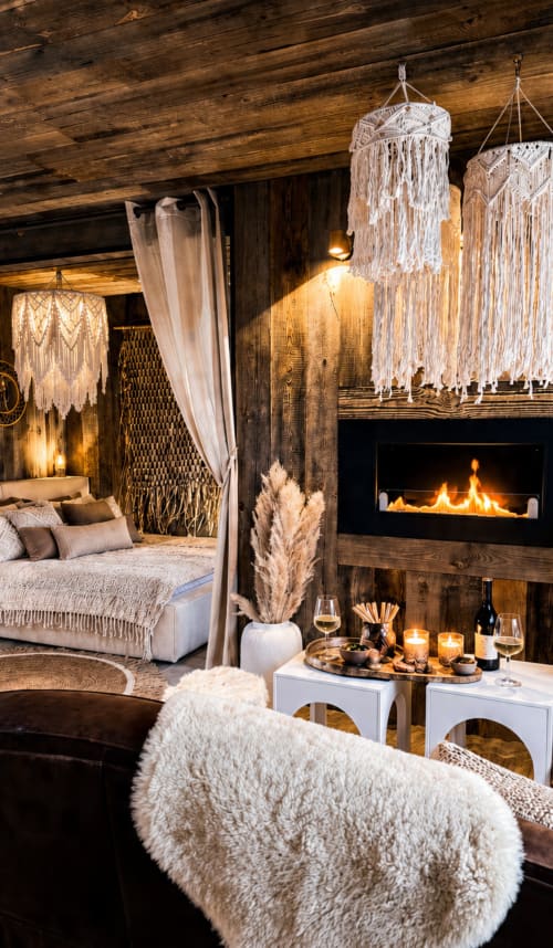 Chambre luxe avec cheminée, décor macramé, textiles douillets et service vin aux Estela Cabanes & Spas