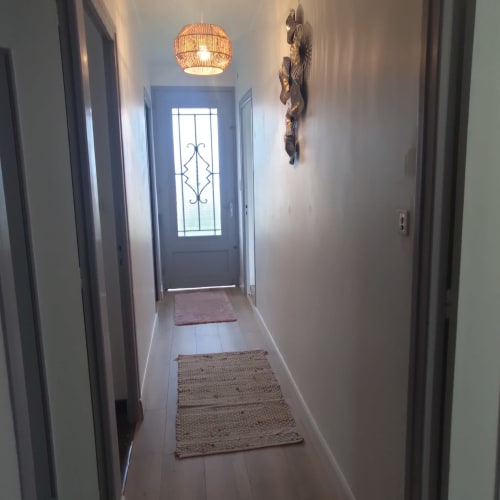 Entrada de corredor iluminada na Maison de Barlest com tapetes tecidos, luminária suspensa e escultura de madeira decorativa na parede