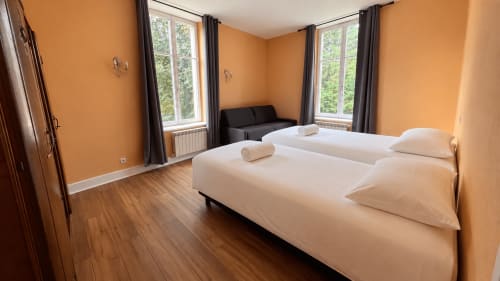 Bright bedroom at Maison Agami with twin beds, orange walls, and large windows overlooking gardens in Rosières aux salines