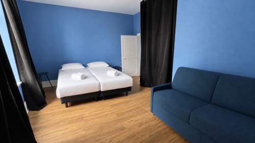 Chambre moderne de la Maison Agami aux murs bleus, deux lits jumeaux avec draps blancs, canapé bleu foncé et parquet