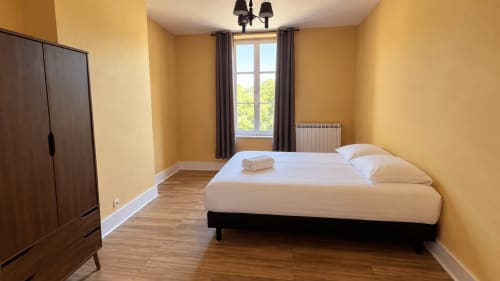 Chambre lumineuse aux murs jaune vif, lit queen, armoire en bois foncé et large fenêtre à la villa Maison Agami à Rosières aux salines