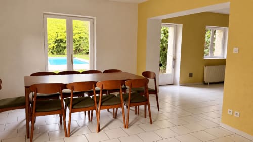 Salle à manger de la villa Maison Agami avec chaises en bois, table, murs jaunes, vue sur la piscine par les portes vitrées, et salon attenant