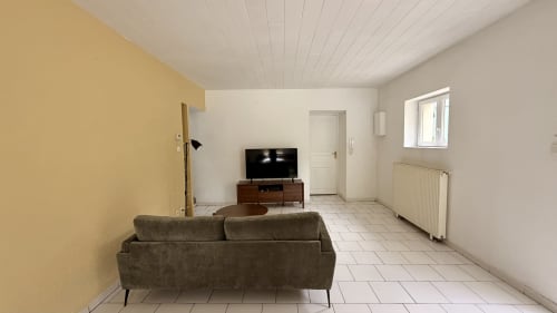 Salon moderne avec canapé gris, téléviseur et mur d'accent jaune à la villa Maison Agami à Rosières aux salines