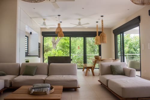 Salon de villa moderne avec canapés baisec, luminaires suspendus tissés et vue panoramique sur le jardin luxuriant à INHÉRENCE