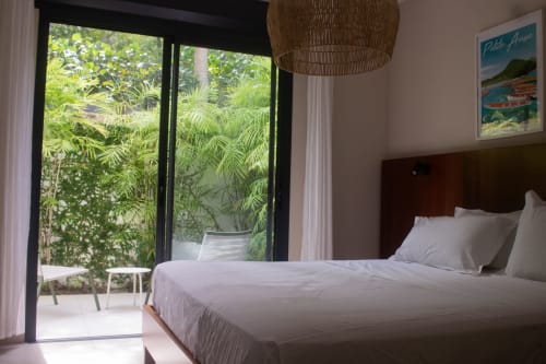 Chambre lumineuse avec lit king-size, vue sur le jardin tropical par les portes vitrées, lampe suspendue tressée à INHÉRENCE, Martinique