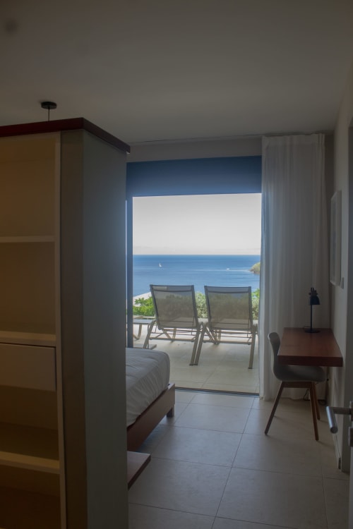 Chambre Villa Mahogany avec balcon vue mer donnant sur les eaux des Caraïbes, chaises longues et voilier aux Anses d'Arlet