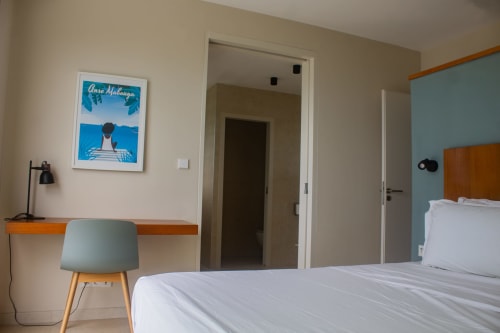 Chambre moderne à INHÉRENCE au Lamentin avec lit blanc, fauteuil turquoise, bureau de travail et œuvres d'art côtières