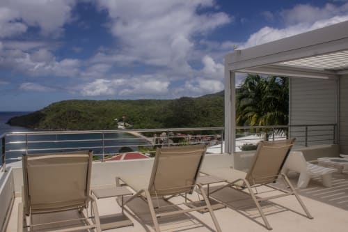 Terrasse luxueuse de l'hôtel INHÉRENCE au Lamentin avec chaises longues donnant sur une baie tropicale et des collines verdoyantes