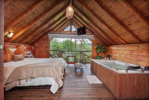Lujosa habitación de cabaña de madera en Sukha Glamping con cama matrimonial, bañera de hidromasaje y vistas al jardín desde el balcón en Rionegro,