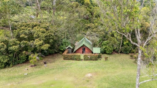 Cabaña glamping roja de madera con techo verde rodeada de exuberantes jardines en Sukha Glamping, Ríonegro