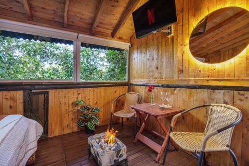 Acogedora terraza de glamping en Sukha con fogata, sillas de mimbre, interior de madera, TV y vistas al jardín en Rionegro, Colombia