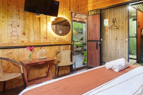 Habitación Eucalipto en Sukha Glamping de Ríonegro con paredes de madera, cama, vista al jardín, TV y acceso a terraza