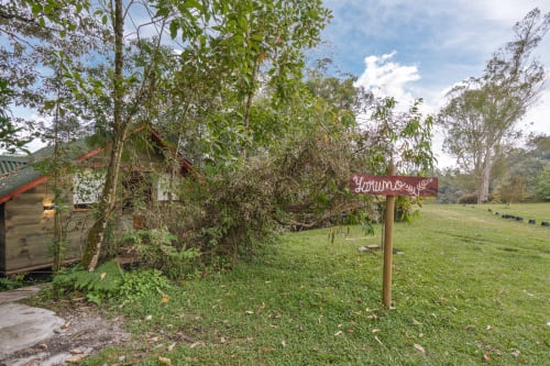 Entrada a la habitación Yarumo en Sukha Glamping de Ríonegro con señalética rústica, jardín circundante y paisaje verde exuberante