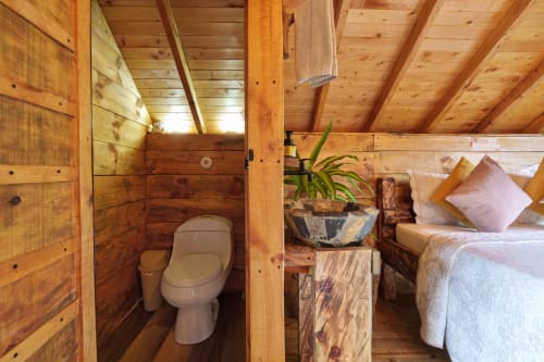 Habitación Yarumo en Sukha Glamping de Ríonegro con interiores de madera, baño privado, cama con almohadas rosas y plantas en macetas