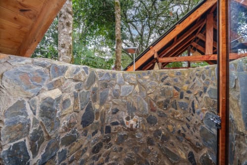 Detalle de muro de piedra en la habitación Yarumo de Sukha Glamping en Ríonegro, Colombia, con vigas de madera y vista al jardín selvático
