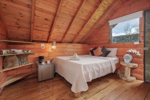 Acogedora habitación de cabaña de madera en Sukha Glamping con cama queen, vigas vistas, ventana con vista al jardín y servicios modernos