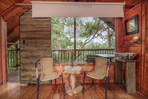 Acogedor balcón de glamping en Sukha con sillas de mimbre, mesa de madera y vistas al jardín de árboles en Rionegro