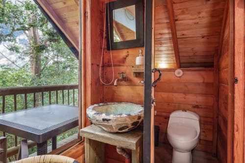 Baño rústico de madera en Sukha Glamping, Ríonegro, con lavabo de piedra natural, inodoro y ducha exterior con vistas al jardín