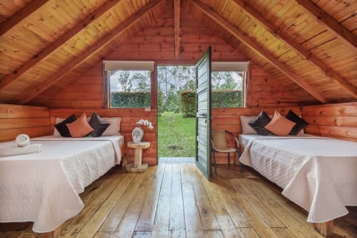 Acogedora habitación de glamping en madera en Sukha con dos camas, vista al jardín y puerta abierta a la terraza en Rionegro
