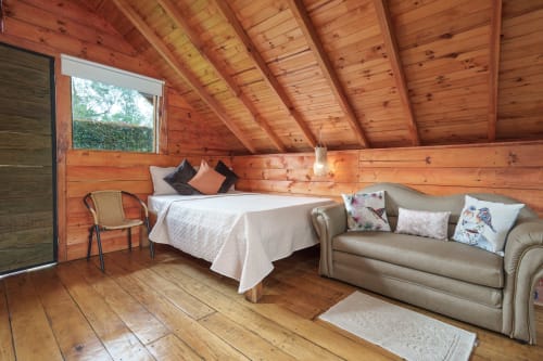 Acogedora habitación de cabaña de madera en Sukha Glamping con cama, sofá y vistas al jardín desde la ventana