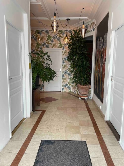 Élégant couloir de La Demeure des Cyprès avec papier peint tropical, plantes en pot, luminaires suspendus et carrelage