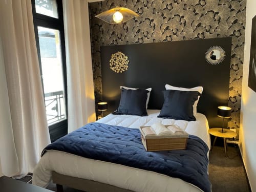 Chambre élégante à La Demeure des Cyprès au centre-ville d'Alençon avec tête de lit foncée, literie bleu marine et papier peint motifs