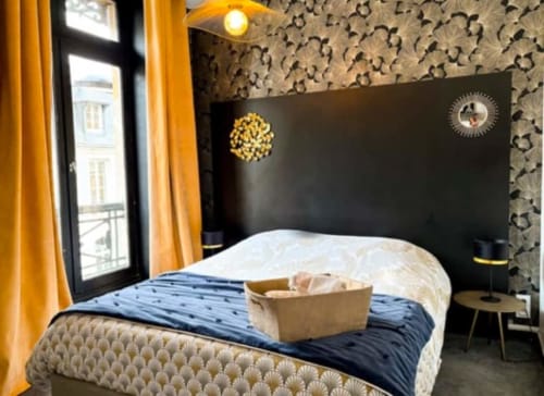 Chambre moderne à La Demeure des Cyprès à Alençon avec accents dorés, tête de lit noire et vue sur la ville