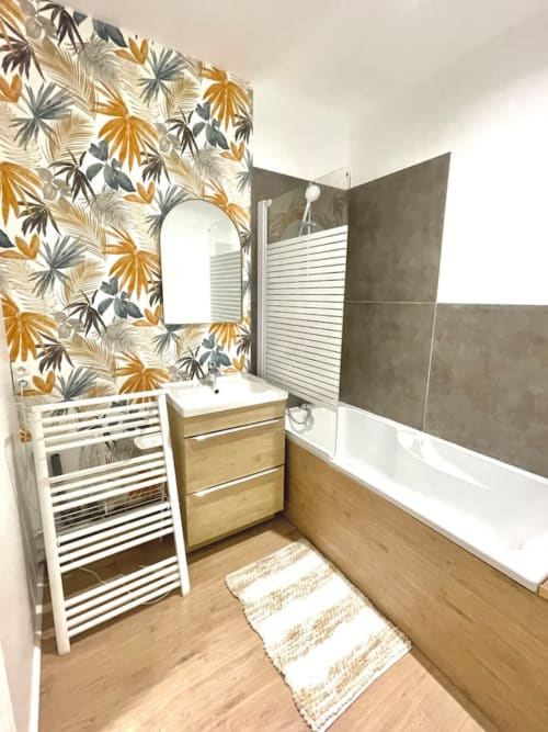 Salle de bain moderne de l'hôtel La Demeure des Cyprès à Alençon avec papier peint botanique, meuble lavabo en bois et baignoire