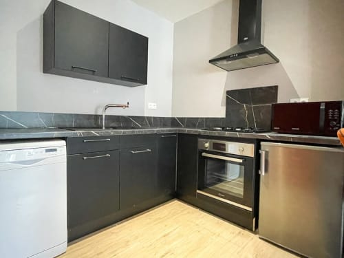 Cuisine moderne noire avec électroménagers en acier inoxydable, dosseret en marbre et parquet dans un appartement du centre-ville d'Alençon