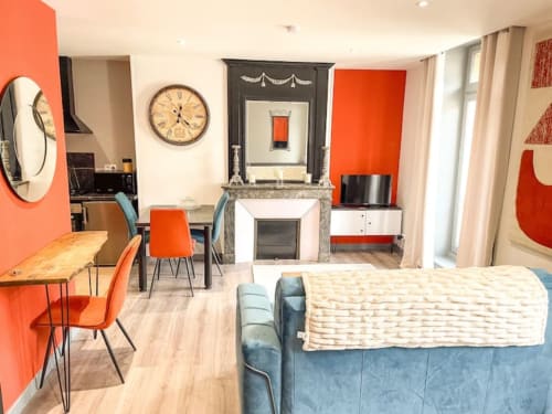 Appartement moderne au centre d'Alençon avec accents orangés, cheminée, salle à manger et canapé bleu à La Demeure des Cyprès