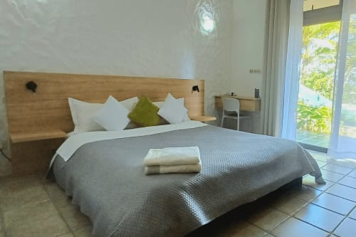 Cosy bedroom at Joubarbe Résidence in Moka with wooden headboard, white pillows, gray bedding, and mountain view terrace