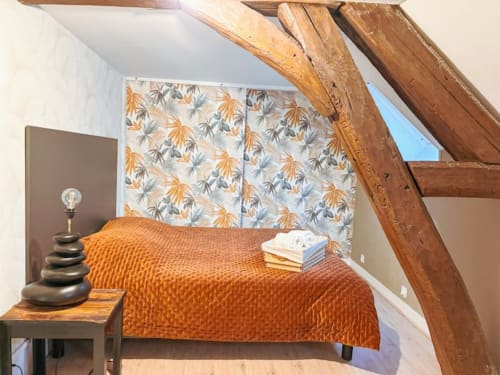 Chambre douillette sous les combles à La Demeure des Cyprès à Alençon avec poutres en bois, literie orange et tête de lit fleurie