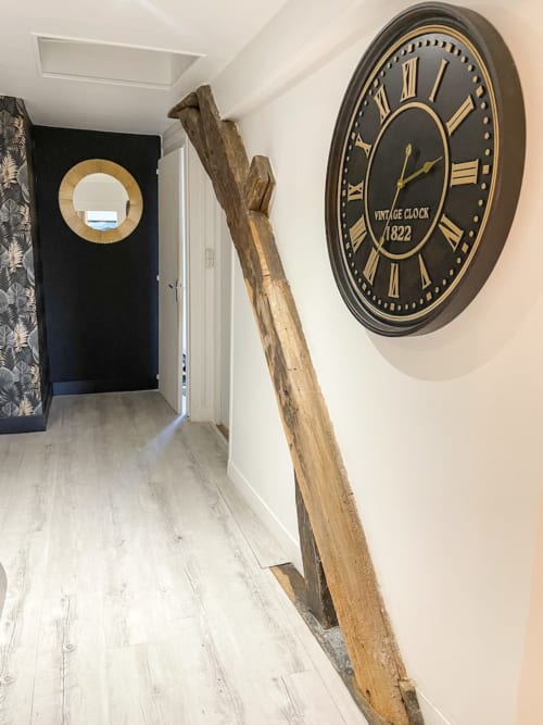 Couloir de La Demeure des Cyprès avec horloge vintage, poutre en bois et miroir dans l'appartement d'Alençon