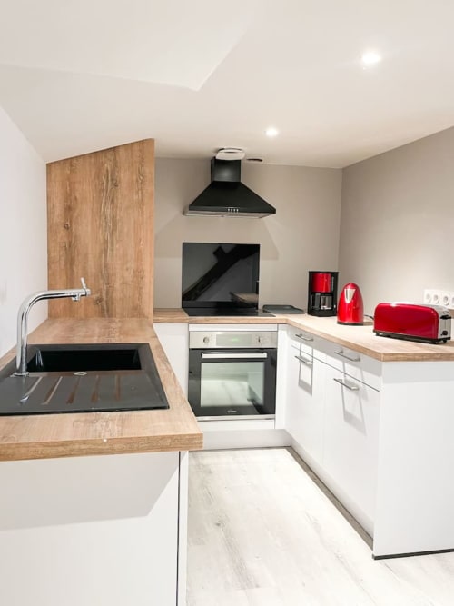 Cuisine moderne à La Demeure des Cyprès, Alençon avec plan de travail en bois, électroménagers noirs et accessoires rouges