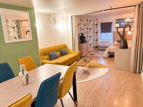 Appartement moderne à La Demeure des Cyprès à Alençon avec canapé jaune, coin repas et chambre décorée de motifs botaniques