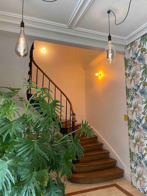 Escalier contemporain aux marches en bois, rampe en métal noir, éclairage suspendu, plantes en pot et papier peint botanique à La
