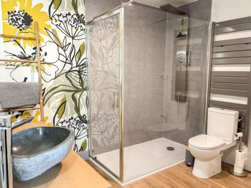 Salle de bain moderne et luxueuse à La Demeure des Cyprès à Alençon : douche vitrée, vasque bleue et œuvre florale