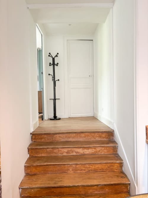 Escalier en bois menant à un élégant couloir aux murs blancs, porte-manteaux noir et porte blanche à La Demeure des Cyprès
