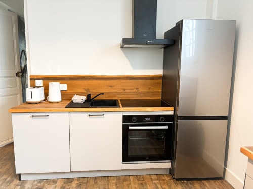 Kitchenette moderne de l'appartement de luxe La Demeure des Cyprès à Alençon, avec mobilier blanc, plan de travail bois et inox