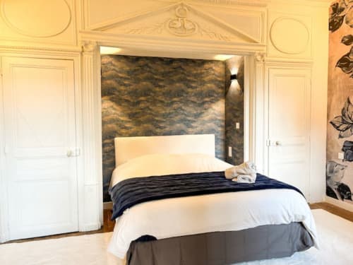 Chambre de luxe à La Demeure des Cyprès avec lit élégant, tête de lit crème, literie foncée et détails architecturaux ornés
