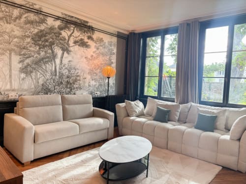 Élégant salon d'appartement de luxe à La Demeure des Cyprès à Alençon avec canapés crème, table en marbre et fresque forêt