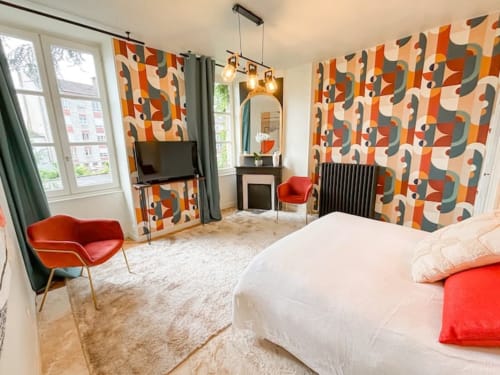 Chambre moderne de La Demeure des Cyprès à Alençon avec papier peint géométrique audacieux, accents rouges et vue sur le jardin