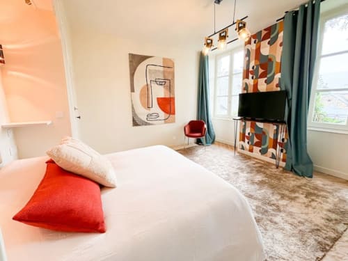 Chambre moderne à La Demeure des Cyprès à Alençon avec lit blanc, accents rouges, art mural abstrait et vue sur le jardin