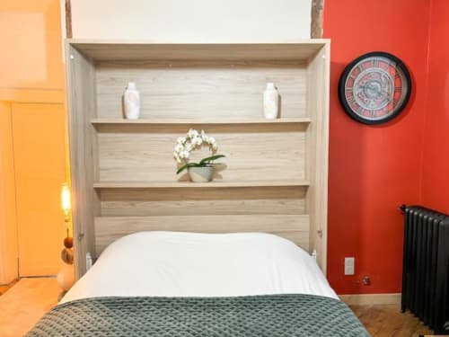 Chambre moderne à La Demeure des Cyprès avec tête de lit en bois clair, oreiller blanc et accents vibrants orange et rouge