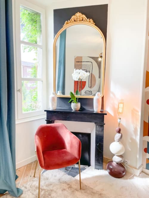 Élégant coin de vanité à La Demeure des Cyprès avec miroir doré ouvragé, cheminée noire, fauteuil en velours rouge et