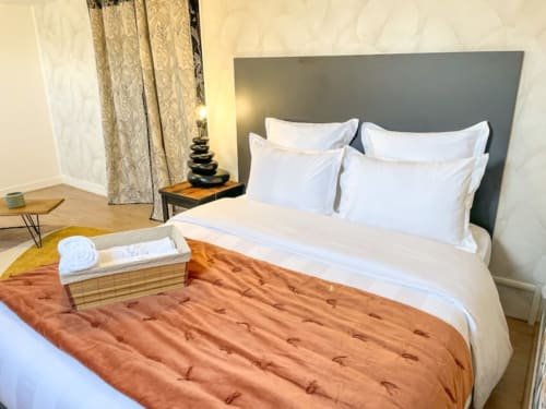 Chambre d'hôtel élégante à La Demeure des Cyprès à Alençon avec oreillers blancs, jeté terracotta, tête de lit grise et ambiance douce