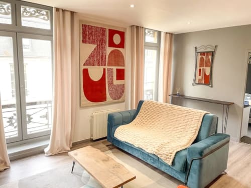 Salon chaleureux à La Demeure des Cyprès à Alençon : canapé bleu canard, plaid crème, art abstrait rouge et décoration moderne.