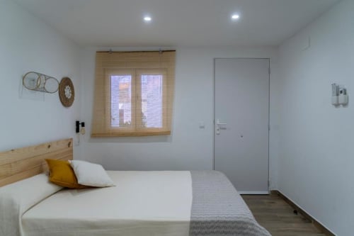 Dormitorio triple luminoso en Cal Xot B&B con cama de madera, almohada amarilla, decoración mural tejida, ventana con persiana de bambú