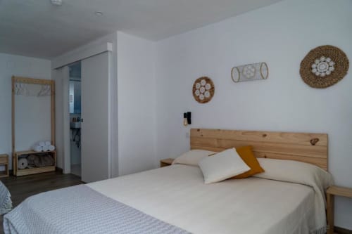 Dormitorio triple luminoso en Cal Xot con cama de madera, sábanas blancas, decoración mural tejida y entrada al baño en Poble Nou
