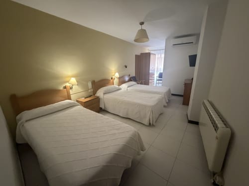 Habitación triple del Hotel JM El Emigrante en Villanueva de la Serena con tres camas, iluminación cálida y vistas a la ciudad